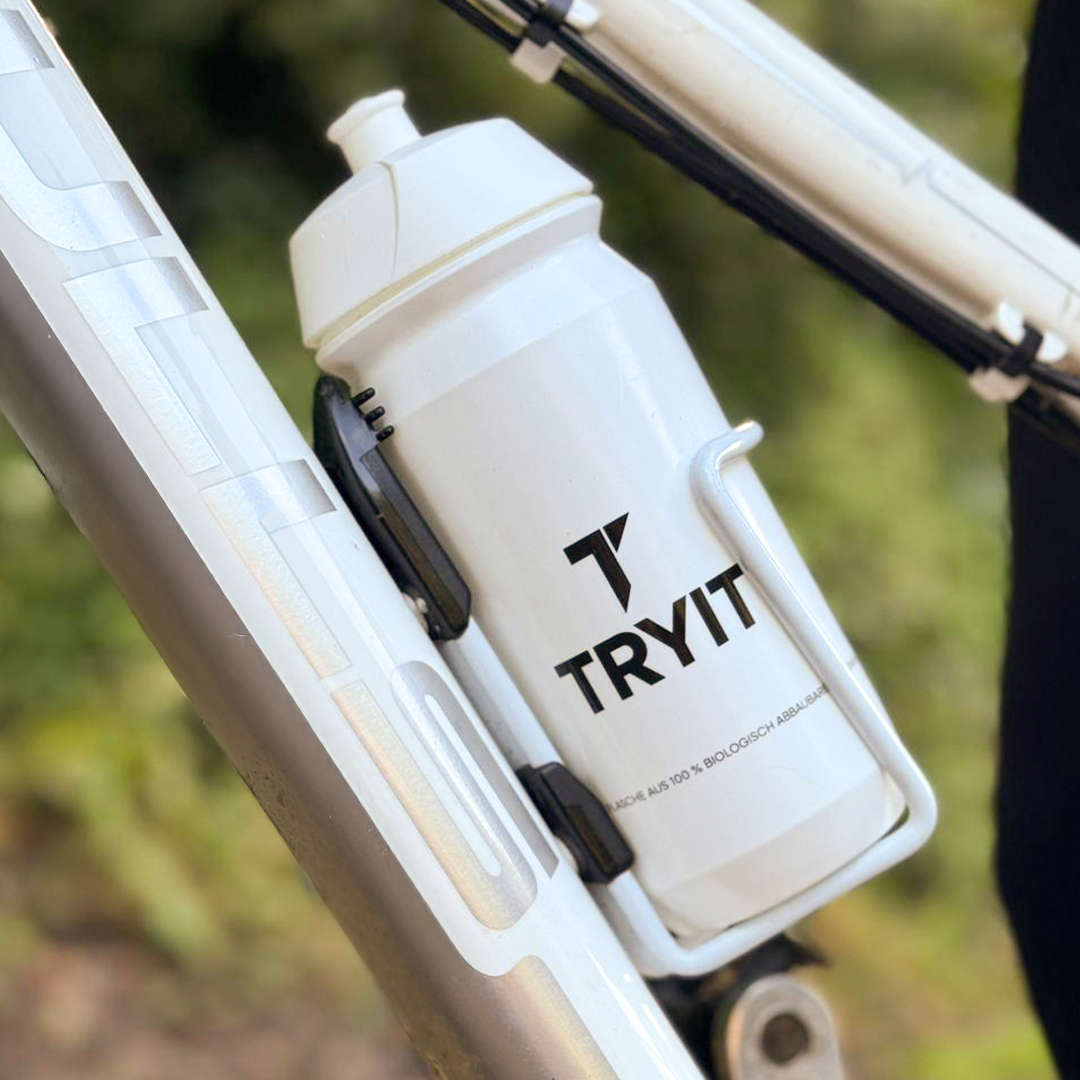 Weiße TRYIT-Trinkflasche mti einem schwarzem TRYIT  in einem passenden Halter, befestigt am weißen Rahmen eines Fahrrads-Logo