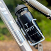 Schwarze TRYIT-Sporttrinkflasche aus recyceltem Material im weißen Flaschenhalter an einem Fahrrad.