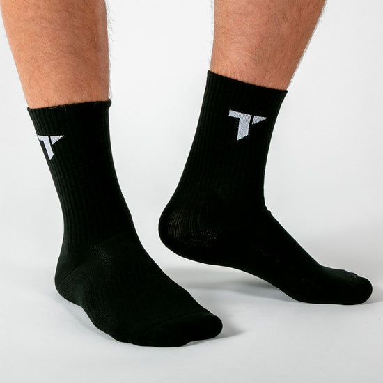 Eine Person trägt ein Paar schwarze Sportsocken mit weißem "T"-Logo von TRYIT an den Knöcheln.