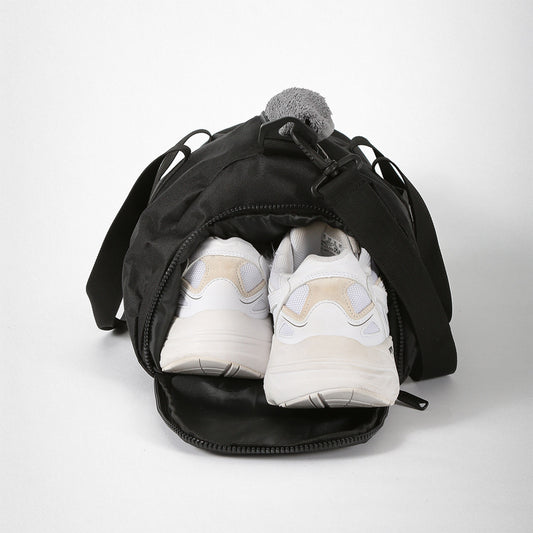 Schwarze Sporttasche mit zwei weißen Turnschuhen, die aus der Reißverschlussöffnung ragen.