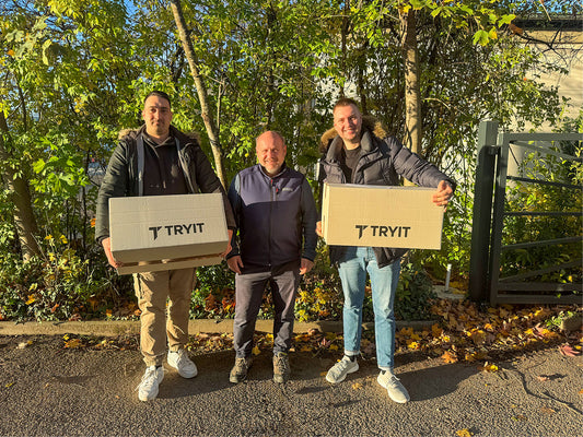 3 Männer in einer Reihe, die beiden Herren links und rechts haben Kartons mit dem Schriftzug "TRYIT" in der Hand und übergeben diese an den Herren in der Mitte