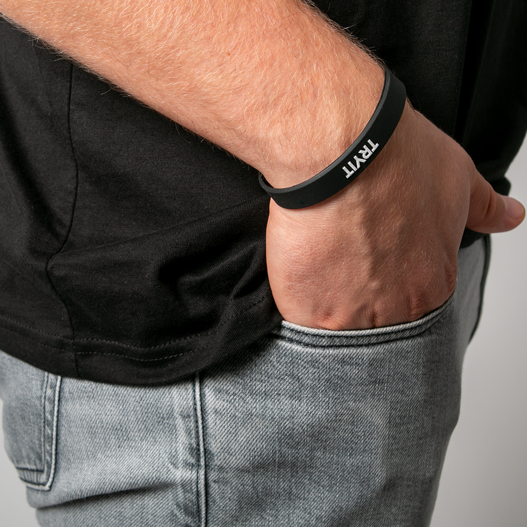 Nahaufnahme eines Mannes in schwarzem T-Shirt und Jeans mit schwarzem Silikonarmband-Armband, auf dem "TRYIT" steht.