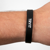 Schwarzes Silikonarmband mit weißem Text "TRYIT" am Handgelenk einer Person