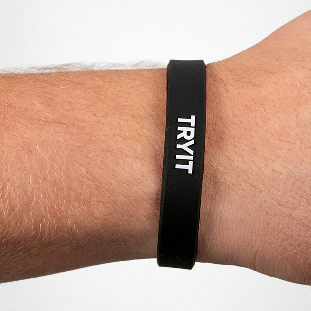 Schwarzes Silikonarmband mit weißem Text "TRYIT" am Handgelenk einer Person
