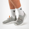 Füße tragen graue Turnschuhe mit weißen Sohlen und weißen Sportsocken mit schwarzem "T"-Logo der Marke TRYIT.