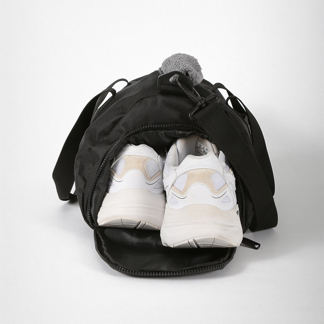 Schwarze Sporttasche mit zwei weißen Turnschuhen, die aus der Reißverschlussöffnung ragen.
